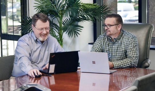 two guys at a desk looking at laptops