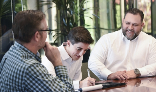 client signing documents surrounded by advisors